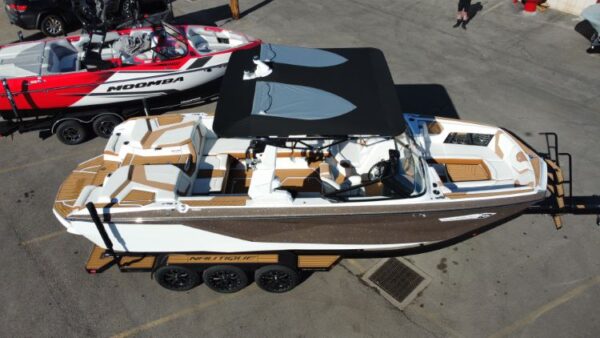 Two motorboats on trailers in a parking lot. One is a red and white Moomba, and the other is a white and brown Nautique with a black canopy.