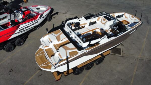 Aerial view of a white and brown motorboat on a trailer next to a red and black speedboat. They are parked on a paved surface.