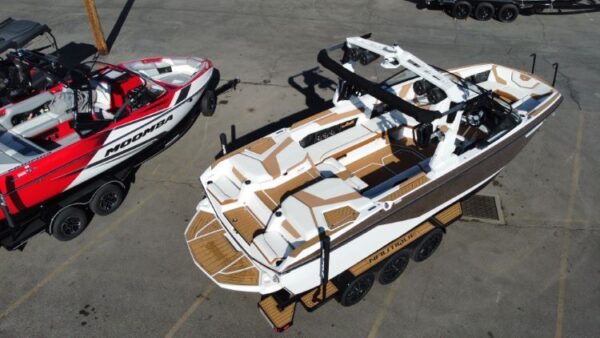 Top view of two boats on trailers in a parking lot. The front boat is white with brown decking, and the rear boat is red and black.