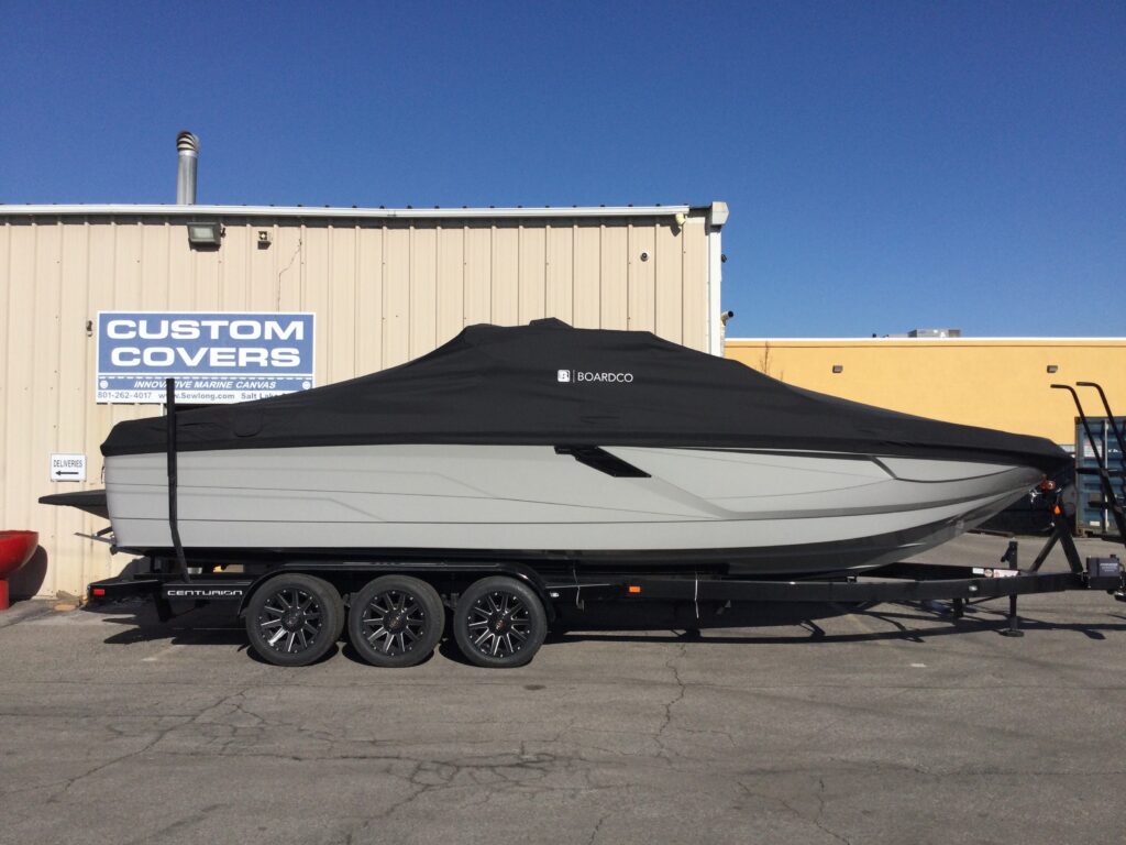 A covered boat on a trailer is parked in front of a building with a sign reading "Custom Covers," showcasing the precision of custom boat covers designed to boost your brand visibility.