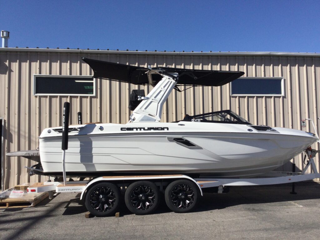 A sleek white Centurion boat rests on a trailer outside a metal building, glistening under the clear blue sky. A SewLong adjustable shade sail provides perfect cover for sun-sensitive gear.