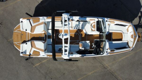 Aerial view of a white and brown motorboat with multiple seats, steering wheel, and controls, parked on a concrete surface.