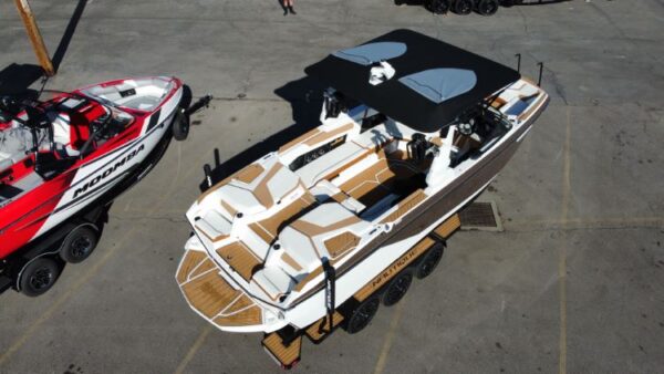 Aerial view of a parked motorboat with white and brown decking, black canopy, and four seats. Adjacent is a partially visible red and white boat with branding.