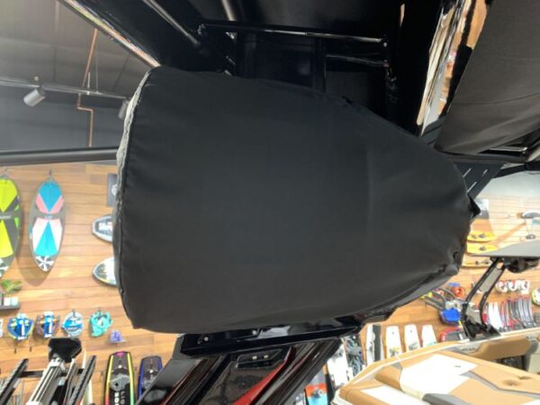 Black speaker cover on a mounted speaker in a store, with various skateboards and surfboards displayed on the wall in the background.