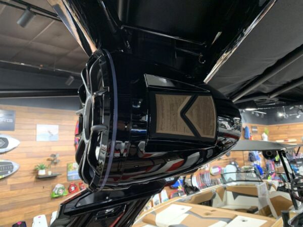 Close-up of a black speaker mounted on a boat, with wooden wall paneling and colorful equipment in the background.