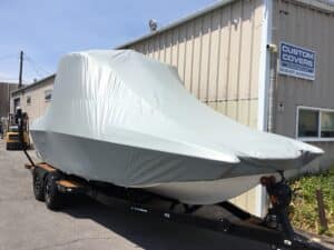 A Malibu 23 MXZ on a trailer, specifically designed for Malibu and Axis Boats, is secured with a custom-fitted Double Up Storage Cover outside a warehouse.