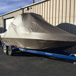 A boat covered with a gray tarp is placed on a blue trailer outside a beige metal building.