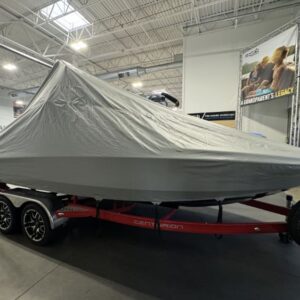 A boat on a red trailer is covered with a gray tarp in a large indoor space with bright lighting.