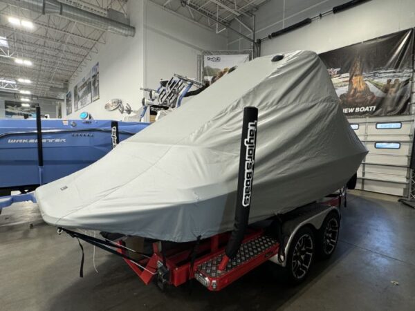 A covered speedboat on a red trailer inside a warehouse, with banners and other boats visible in the background.