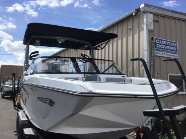 A white boat on a trailer at a custom covers shop, with a canopy and sleek design, parked outside a metal building under a blue sky.