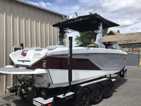 A white and maroon boat sits on a trailer outside a metal building.