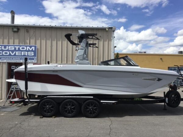 A white and maroon speedboat on a triple-axle trailer parked outside a building with a sign reading "Custom Covers.