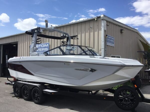 A white and maroon motorboat on a trailer parked outside a metal building under a partly cloudy sky.