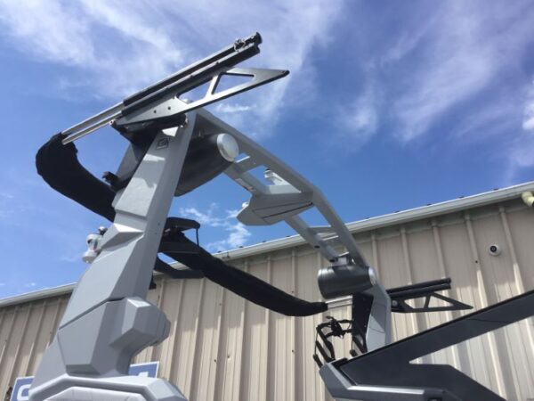 A futuristic machine with metal arms and components against a blue sky backdrop, next to a metal building.