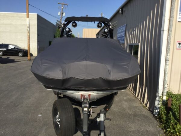 A boat with a gray cover is parked on a trailer outside a warehouse.