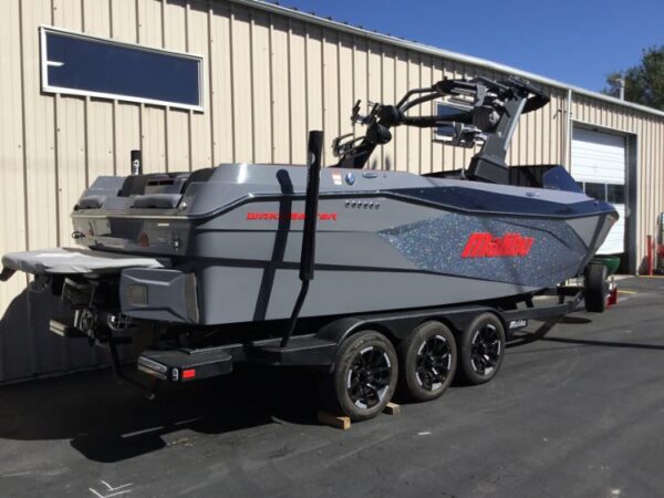 A parked gray Malibu Wakesetter boat on a trailer outside a beige warehouse building.