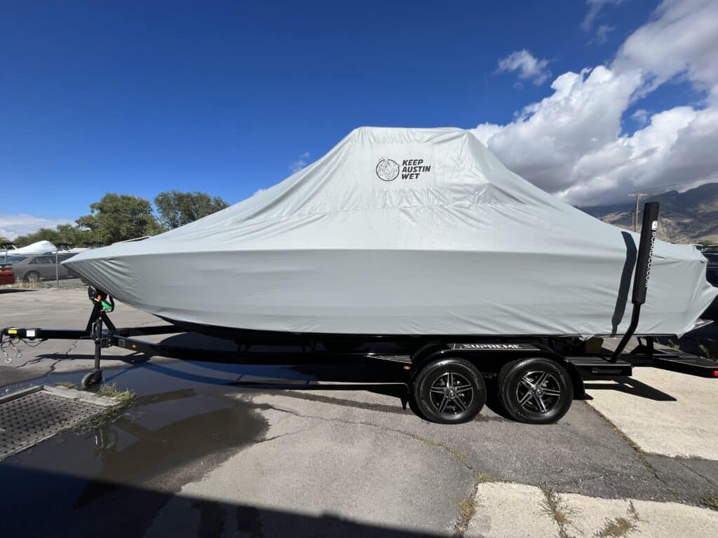 A covered boat, sporting a custom cover with the words "Keep Austin Wet," is parked on a trailer at a lot. This unique touchpoint boosts brand visibility while keeping the vessel protected.