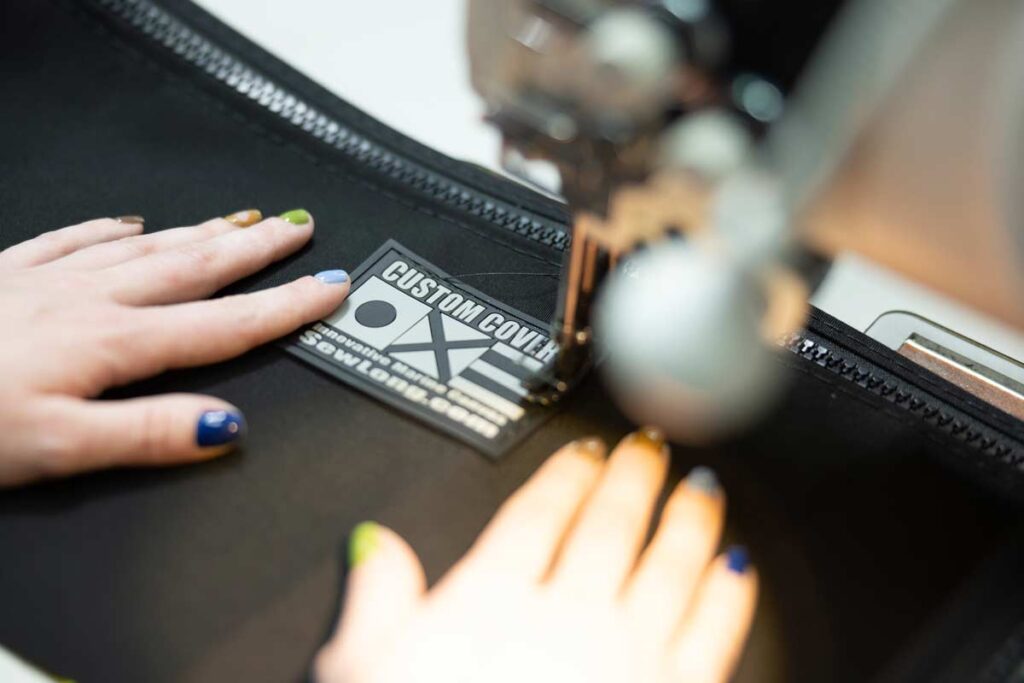 Hands expertly guide fabric through a sewing machine, stitching a label that reads "Custom Cover," showcasing the precision and quality expected from an OEM.