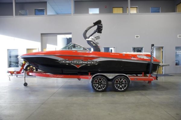 A red and black Centurion boat on a trailer in a showroom.