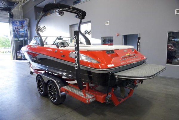 Red and black sport boat with tower on a trailer in an indoor showroom setting.